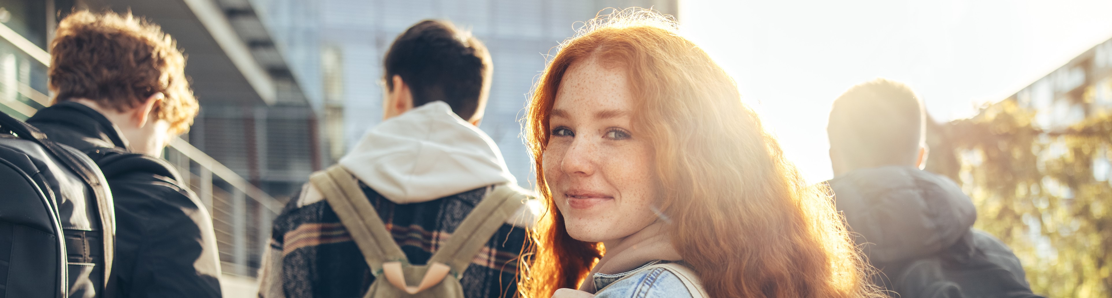 mehrere Jugendliche von hinten fotografiert, eine junge Frau dreht sich lächelnd um
