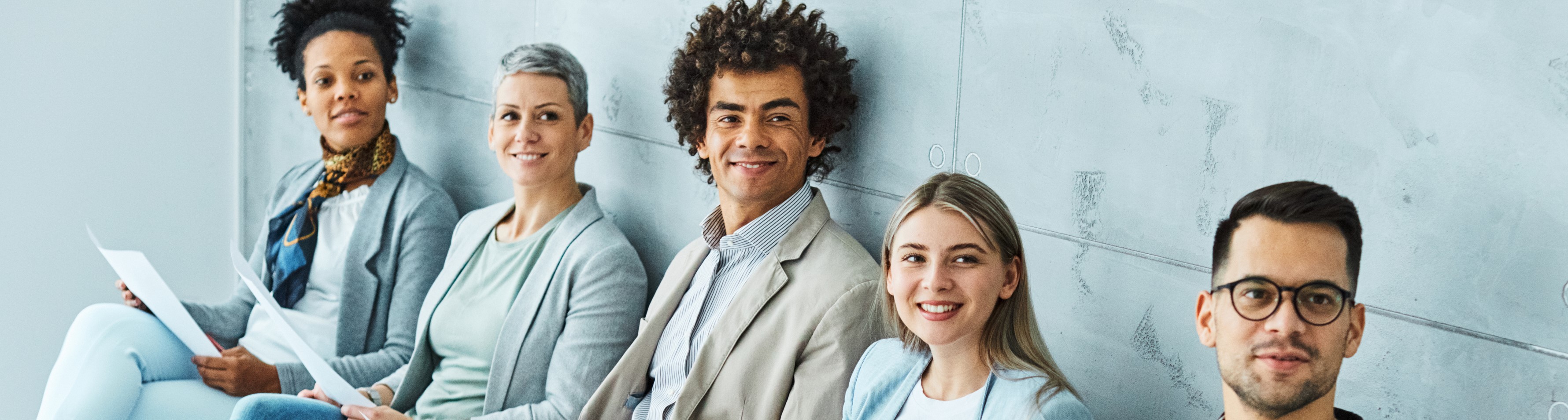5 Menschen in heller Businesskleidung, nebeneinander sitzend