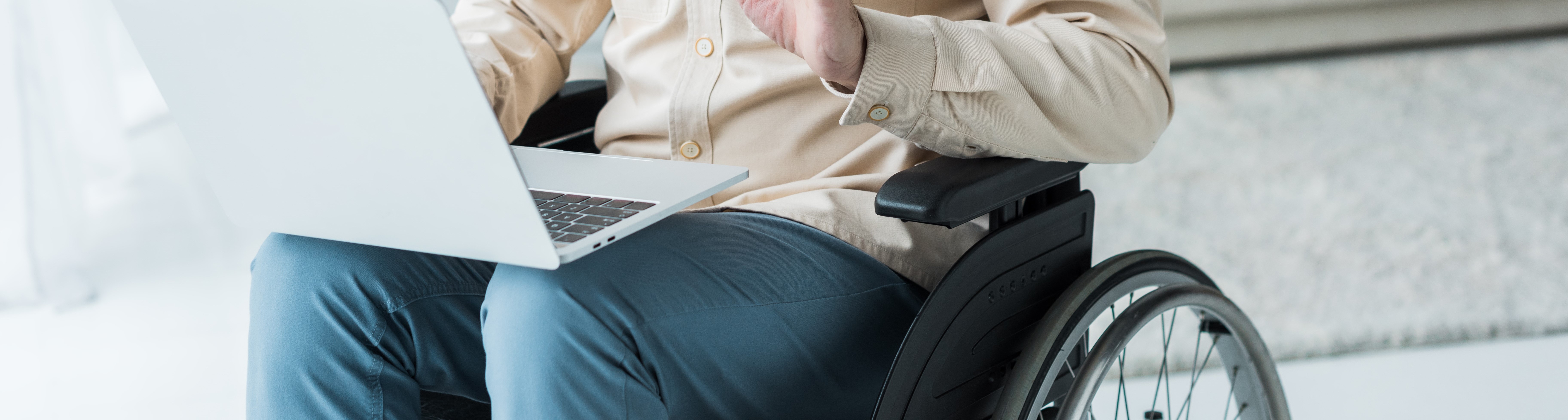 Mann mit Laptop in Jeans und Hemd im Rollstuhl, nur Körpermitte sichtbar