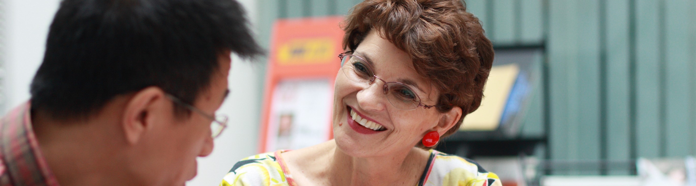 Frau mit Brille und dunklen Haaren lacht einen Mann mit Brille und dunklen Haaren an